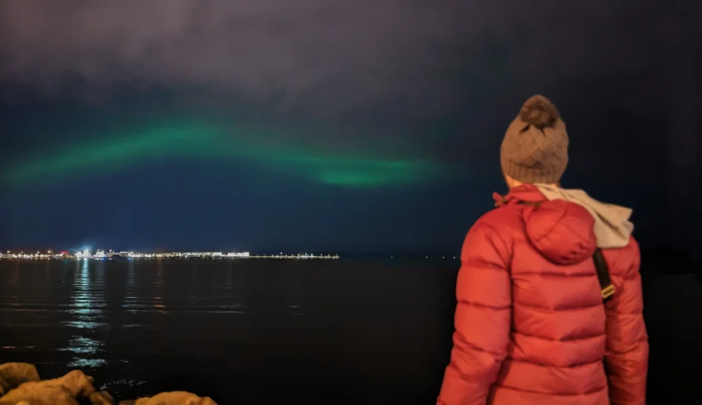 Woman looking at northern lights across Reykjavík harbour